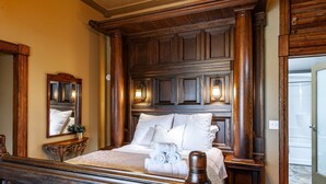 Ein traditionell eingerichtetes Schlafzimmer mit einem hölzernen Kopfteil, einem großen Bett mit weißer Bettwäsche, einem Nachttisch mit Lampe und einem Spiegel.