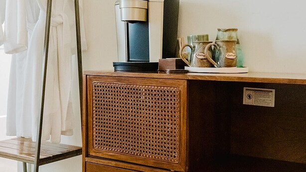 A wooden cabinet with a woven front panel, a coffee maker, and a mug on top. - Wild Iris Room at The Wildflower Inn (Gold Beach)