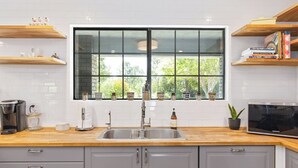 Una cocina con un ventanal grande, un lavamanos de acero inoxidable, estantes de madera y un microondas.