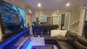 Ein modernes Wohnzimmer mit einem großen Flachbildfernseher, einer schwarzen Ledersofa, einem weißen Teppich und einer Bar mit Hockern.