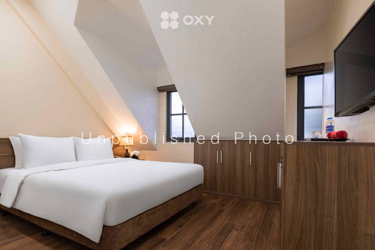 A bedroom with a bed, wooden wardrobe, and a TV on a stand.
