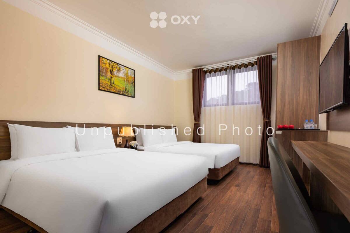A hotel room with two beds, a flat-screen TV, wooden flooring, and a painting on the wall.