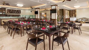 A spacious dining area with multiple tables and chairs, a kitchen in the background, and a modern chandelier. - Ha Long Essence Classic Hotel (Bai Chay)