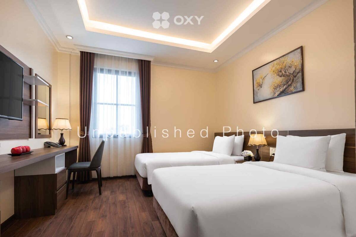 A hotel room with two beds, a desk with a chair, a TV, and a painting on the wall.