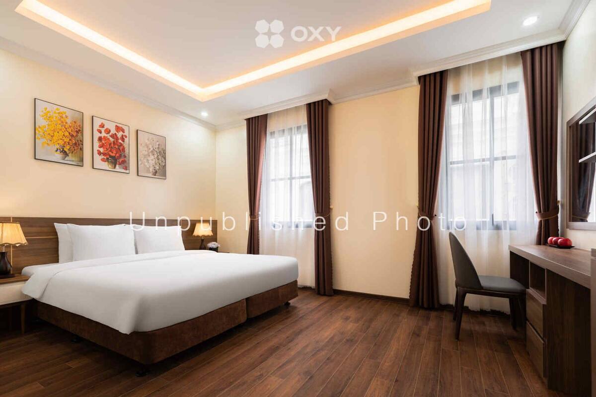 A hotel room with a large bed, a desk, and a chair. There are curtains on the windows, and artwork on the walls.