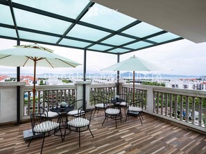 A balcony with a glass ceiling, wooden flooring, and outdoor furniture. - Ha Long Essence Classic Hotel (Bai Chay)