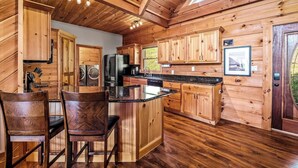 Interior de una cabaña de madera con cocina, comedor y un gran ventanal.