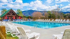 Una piscina con sillones de descanso, un edificio de madera con sombrillas rojas y montañas al fondo.