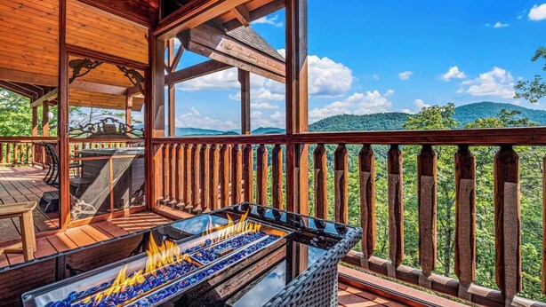 Una terraza de madera con zona de barbacoa de vidrio y vistas a un paisaje montañoso.