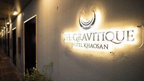 Un letrero de hotel con el nombre "The Gravitative Hotel Khansom" iluminado sobre una pared con textura.
