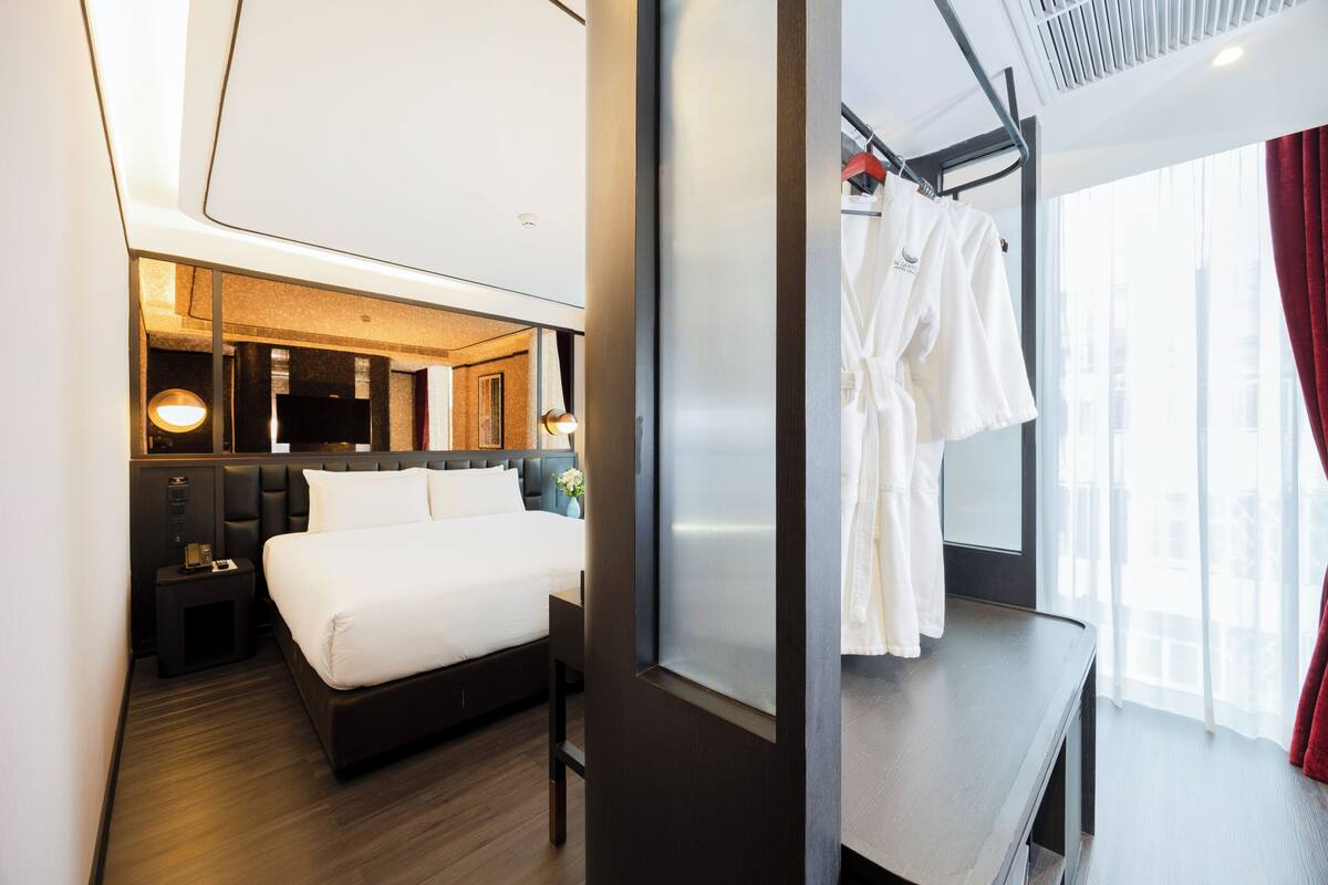A modern hotel room with a large bed, a bedside table, a mirror, and a window with curtains.