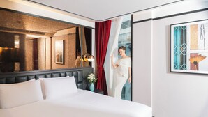 Habitación de hotel con una cama grande, un espejo, una cortina roja, una obra de arte enmarcada y un jarrón con flores.
