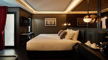 A hotel room with a large bed, a bedside table with a lamp, a mirror, and a framed picture on the wall.