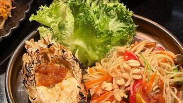 A variety of dishes including grilled lobster, noodles, and a salad with vegetables and peanuts.