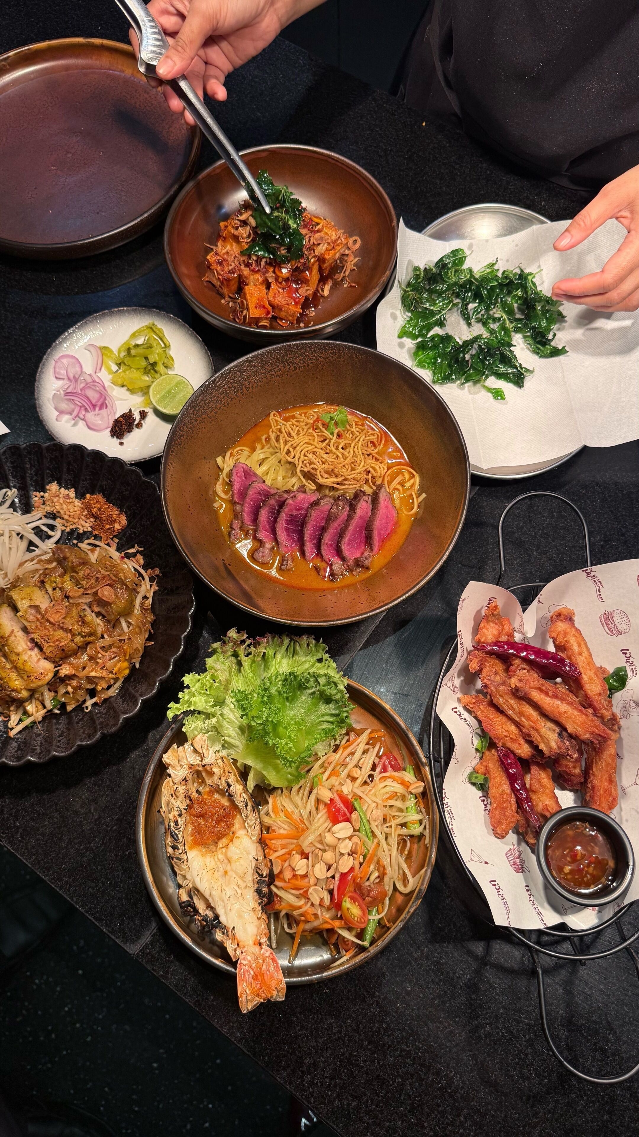 Une variété de plats sont disposés sur la table, notamment des nouilles, de la viande et des légumes.