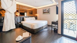 Habitación de hotel con cama, mesitas de noche, escritorio, silla, bata colgada y ventana con diseño geométrico.