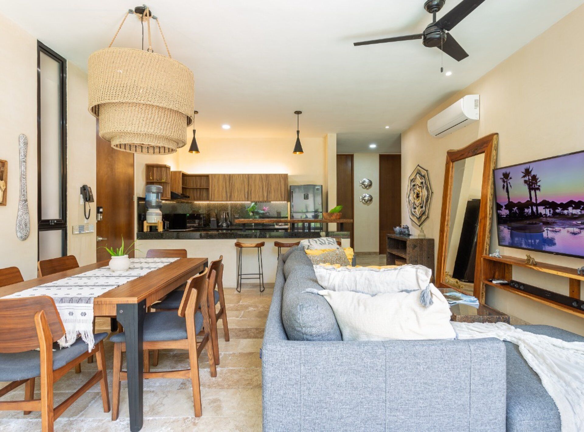 A modern living room with a grey sofa, wooden dining table, and a kitchen in the background.