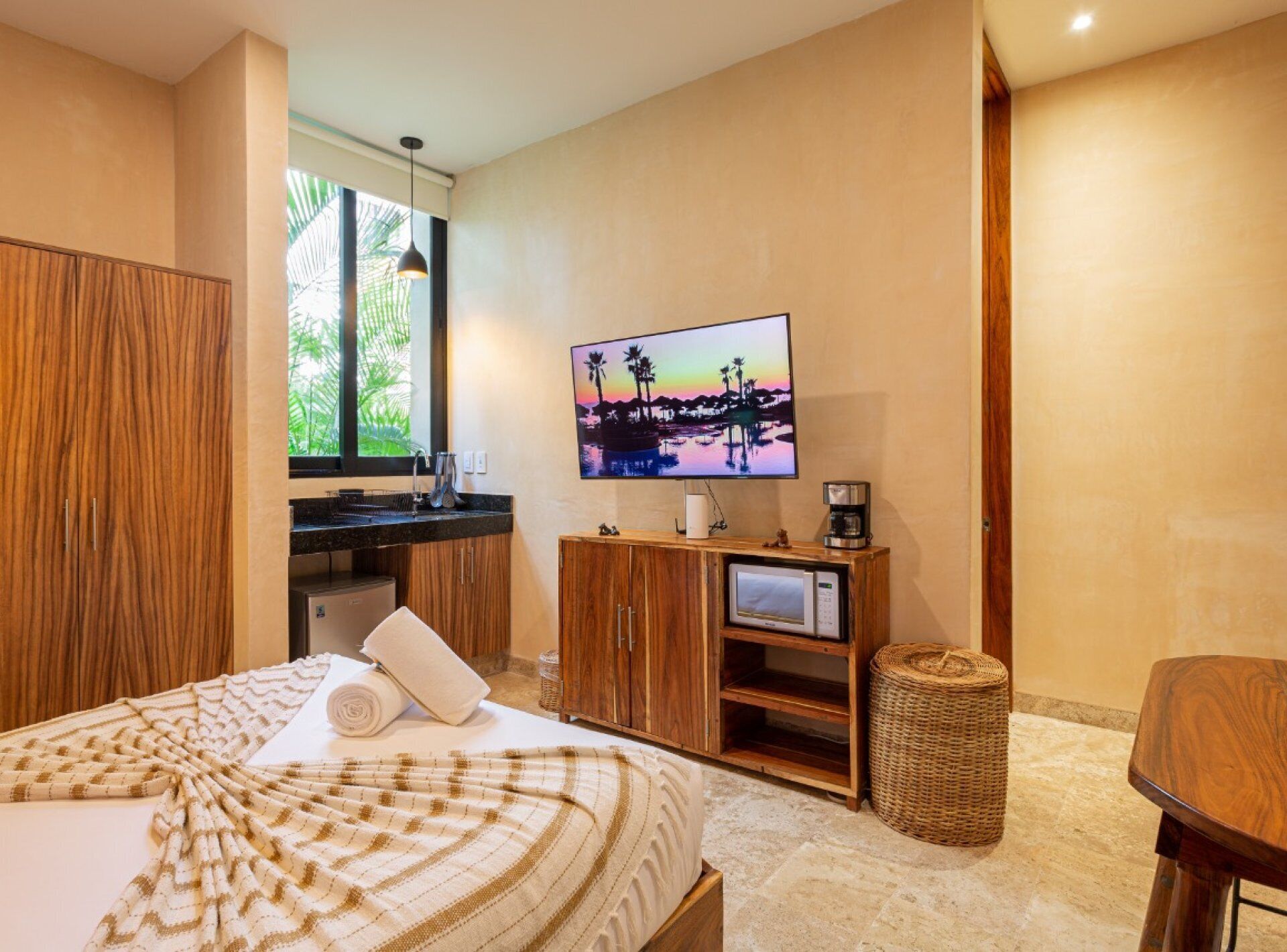 A hotel room with a bed, a TV, a coffee maker, and a small kitchenette.