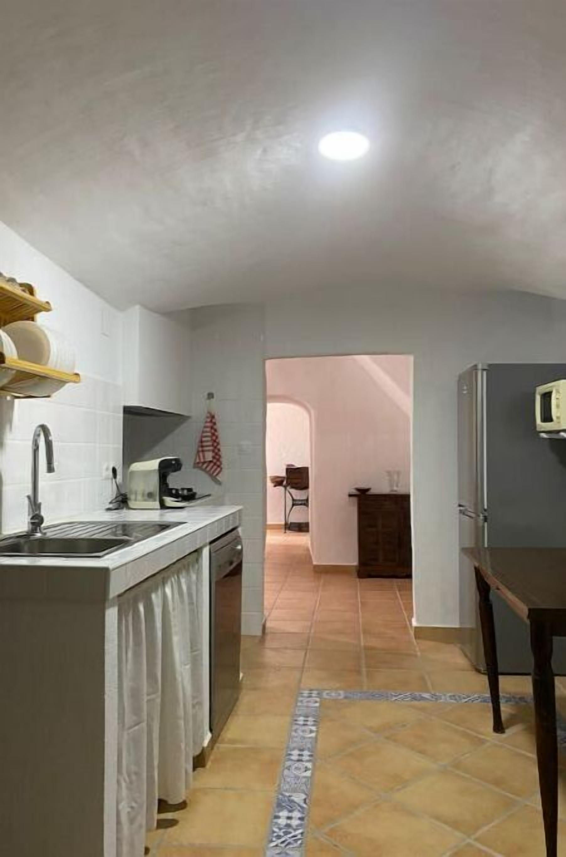 A kitchen with a sink, stove, and refrigerator. There is a tiled floor and a doorway leading to another room.