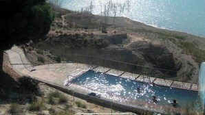 Una piscina amb vista al mar, envoltada de terreny rocos i vegetació escassa.