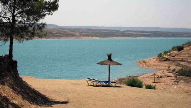 Una platja amb una vista clara de l'aigua, un para-sol de palla i una cadira relax.