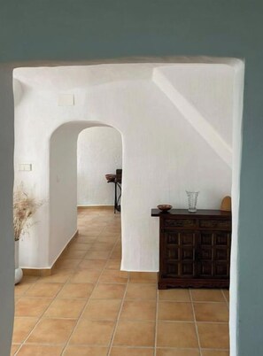 An interior corridor with a tiled floor, a wooden cabinet, and a doorway leading to another room. - Cueva de Ramón y Elvira (Cuevas del Campo)