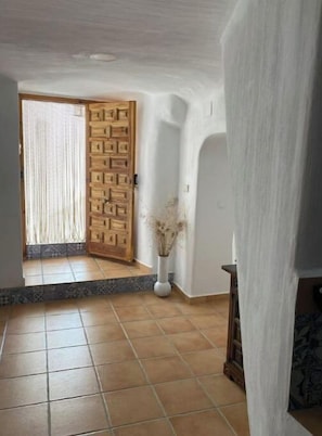 A hallway with a wooden door, a vase with dried plants, and a tiled floor. - Cueva de Ramón y Elvira (Cuevas del Campo)