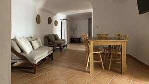 Àmplia zona d'estar amb un sofà, una taula de dinar i cadires, i un televisor penjat a la paret.
