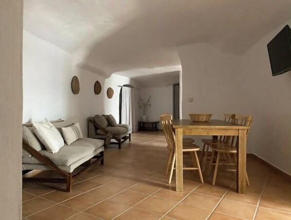 A spacious living area with a sofa, a dining table with chairs, and a TV mounted on the wall.