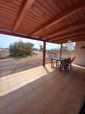 A covered patio with a table and chairs, a view of a desert landscape, and a wooden ceiling. - Relax on the beach (la oliva)