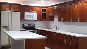 Una cocina moderna con armarios de madera, encimera blanca, microondas integrado y pileta de acero inoxidable.