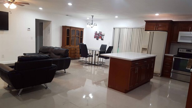 Una sala de estar moderna con sofá, mesa de comedor, sillas y una zona de cocina con refrigerador y horno.