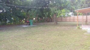 Patio trasero con terraza de madera, una parrilla y un bote de basura verde.