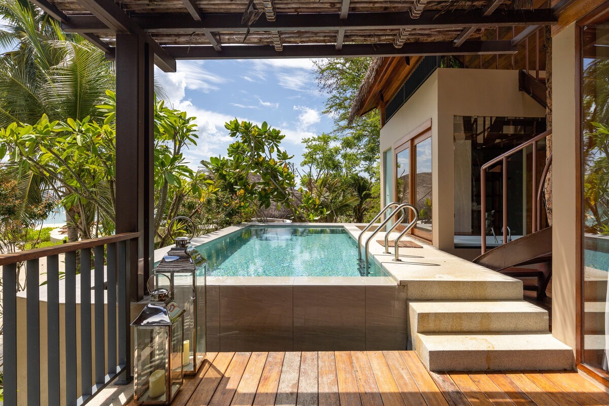 A pool with steps leading up to it, surrounded by wooden decking and glass railings.