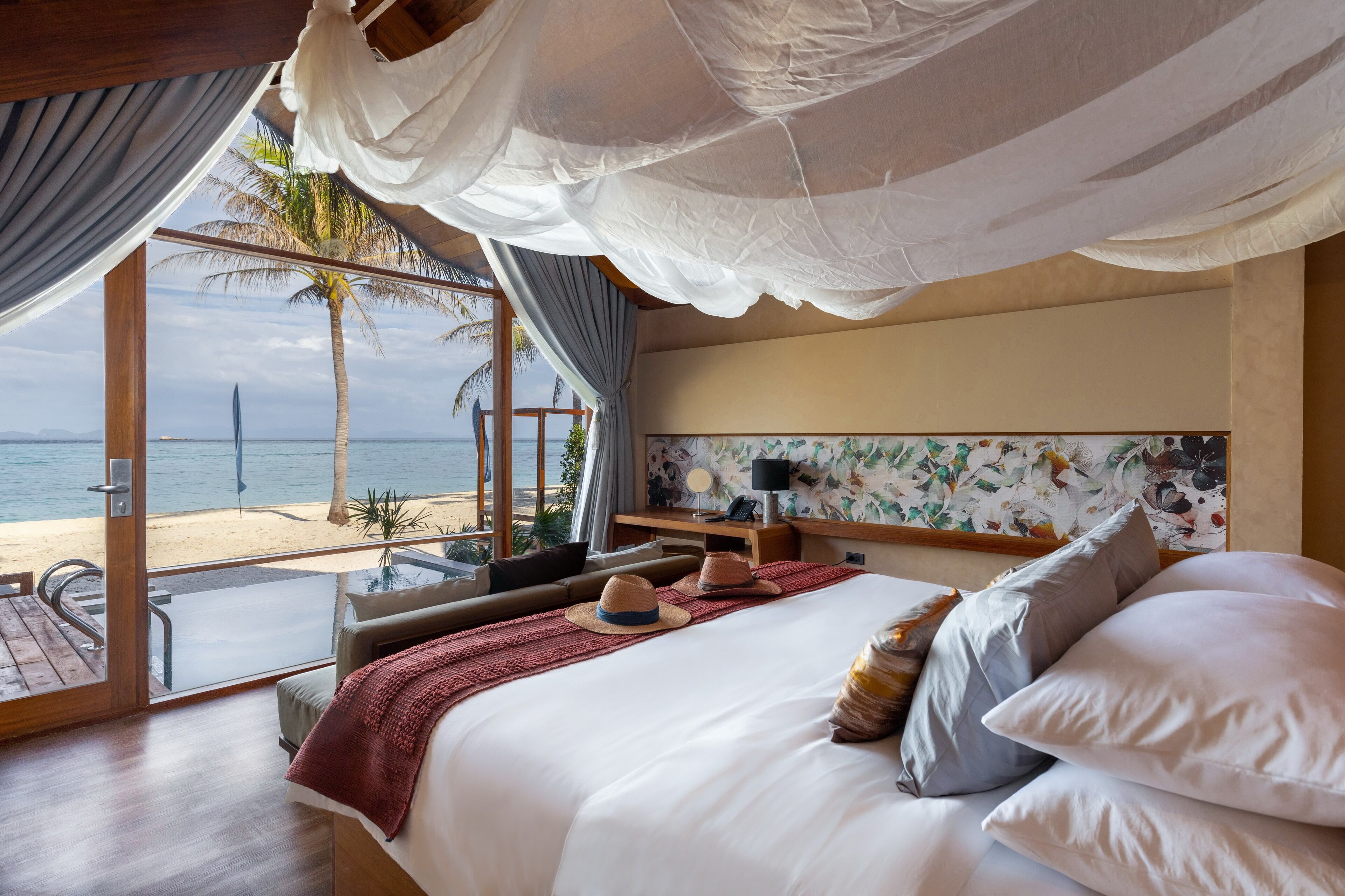A bedroom with a large bed, a view of the beach, and a balcony with a table and chairs.