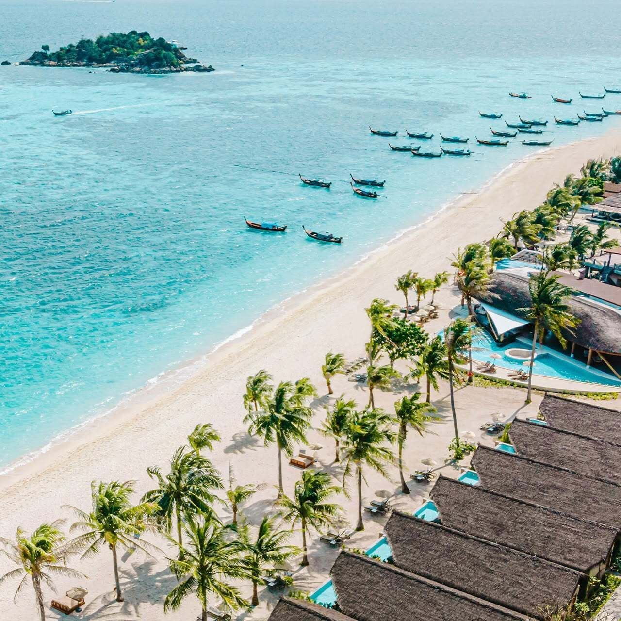 Un resort en la playa con piscina, palmeras y barcos en el agua.