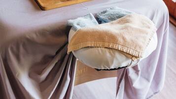 A bed with a wooden tray holding a massage tool and a flower, a towel, and a small bowl with a flower on a bedside table.