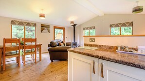 A kitchen with a granite countertop, wooden cabinets, and a dining area with a table and chairs. - Deluxe lodge with one master double with en suite walk-in shower and one twin. (Cartmel)
