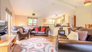 A living room with leather sofas, a wooden coffee table, and a kitchen in the background.
