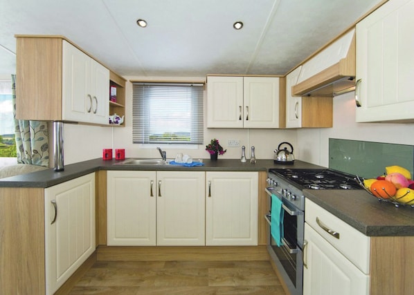 A compact kitchen with white cabinets, a gas stove, a sink, and a window with blinds.
