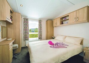 A hotel room with a bed, a desk, a chair, a window with curtains, and a view of the outdoors.