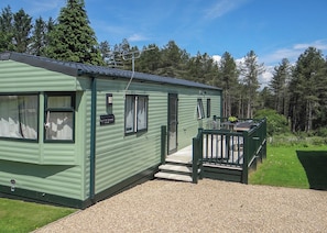 A green mobile home with a porch, a small deck, and a gravel driveway. - Comfortable and spacious 12ft-wide caravan with one double and one twin. (Slaley, Hexham)