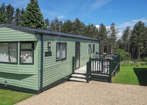 A green mobile home with a porch, a small deck, and a gravel driveway.