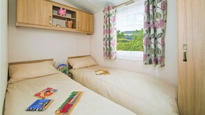 Une chambre avec deux lits, une armoire en bois et une fenêtre ornée de rideaux à motifs floraux.
