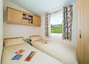 A bedroom with two beds, a wooden cabinet, and a window with floral curtains.