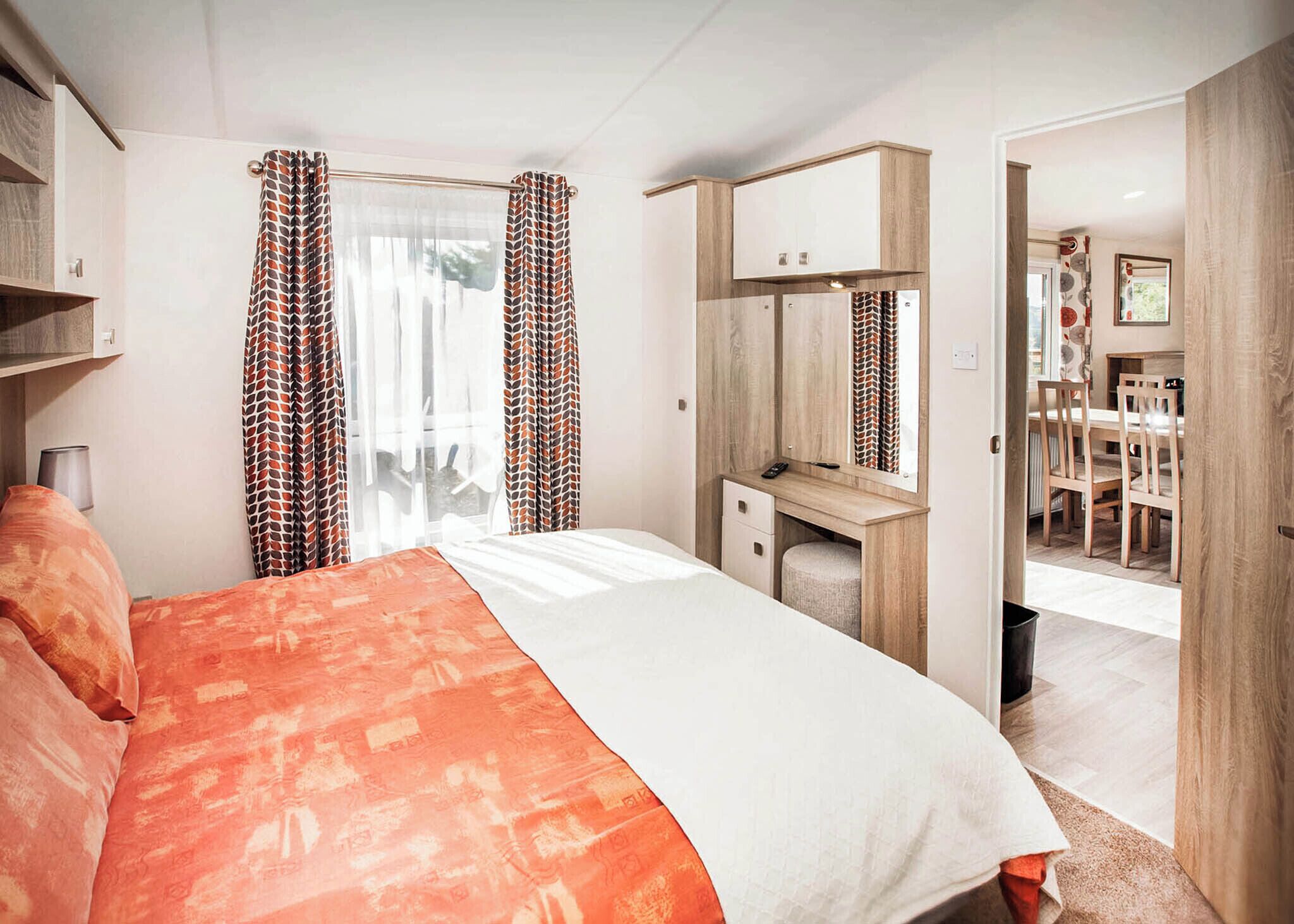 Ein Schlafzimmer mit Bett, Schreibtisch, Spiegel und Blick in einen Essbereich.