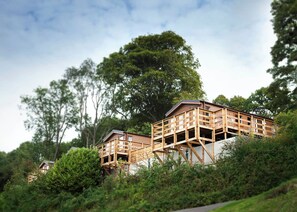 Een houten chalet met een balkon, omgeven door weelderige begroeiing en bomen.