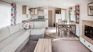 Un salon moderne comprenant un canapé, une table à manger et des chaises, un coin cuisine équipé d’appareils électroménagers et une cheminée.