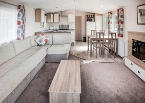 A modern living room with a sofa, a dining table, and chairs, a kitchen area with appliances, and a fireplace. - The Maple is designed to give you an all inclusive spec at an affordable price. (Tenbury Wells)