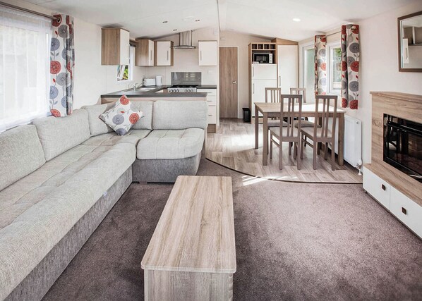 A modern living room with a sofa, a dining table, and chairs, a kitchen area with appliances, and a fireplace. - The Maple is designed to give you an all inclusive spec at an affordable price. (Tenbury Wells)